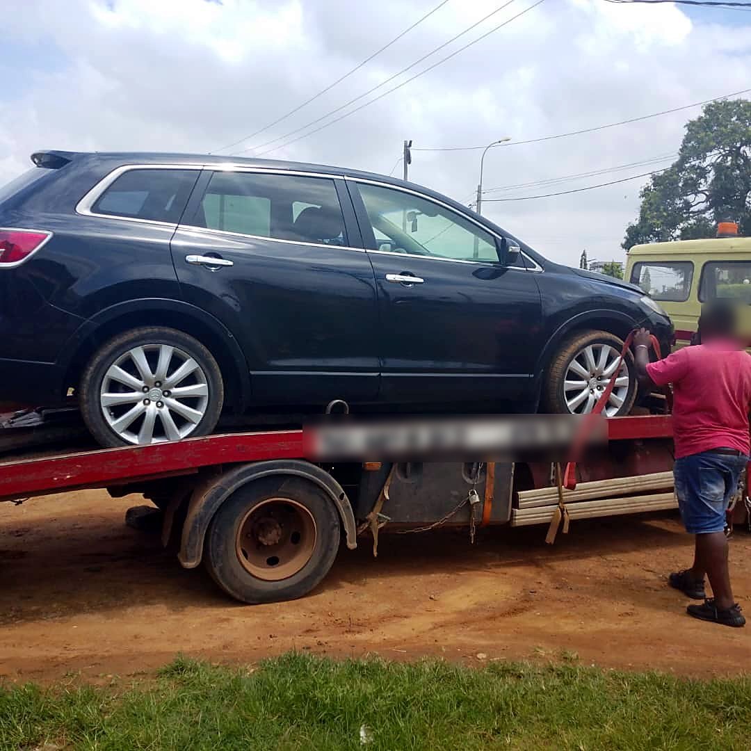 Dépanneur fixant les sangles d’un SUV Mazda CX-9 noir sur le plateau, à Bonabéri