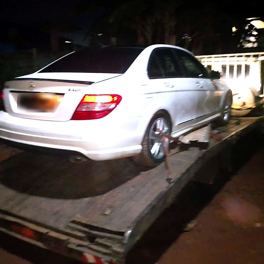 Vue arrière d’une Mercedes Classe C blanche sanglée sur le plateau de la dépanneuse, de nuit à New Bell